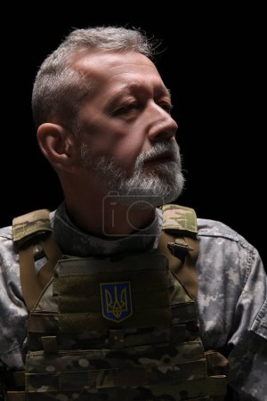 Foto de Soldado maduro con parche de escudo de armas ucraniano sobre fondo oscuro, primer plano - Imagen libre de derechos