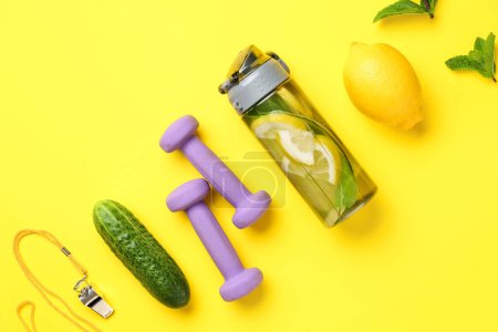 Téléchargez les photos : Bouteille de limonade sportive avec concombre et haltères sur fond jaune - en image libre de droit