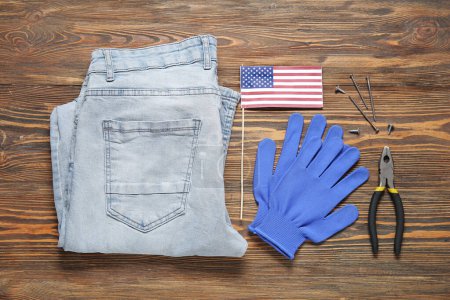 Téléchargez les photos : Jeans pantalon avec drapeau des États-Unis, gants et fournitures de construction sur fond en bois. Fête du travail - en image libre de droit