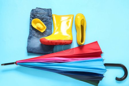 Foto de Botas de goma amarillas con jeans y paraguas sobre fondo azul - Imagen libre de derechos