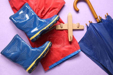 Foto de Botas de goma azules con chaqueta, paraguas y avión de juguete sobre fondo lila - Imagen libre de derechos