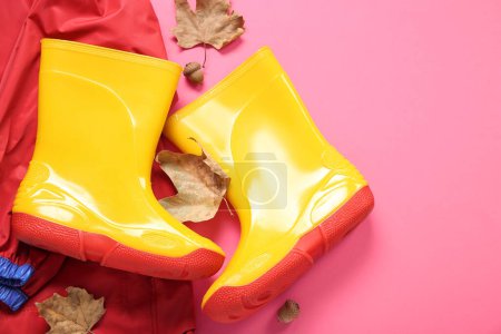 Foto de Botas de goma amarillas con chaqueta y hojas de otoño sobre fondo rosa - Imagen libre de derechos