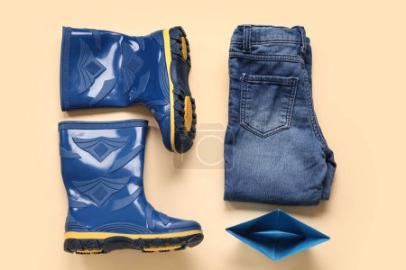 Foto de Botas de goma azules con jeans y barco de papel sobre fondo amarillo - Imagen libre de derechos