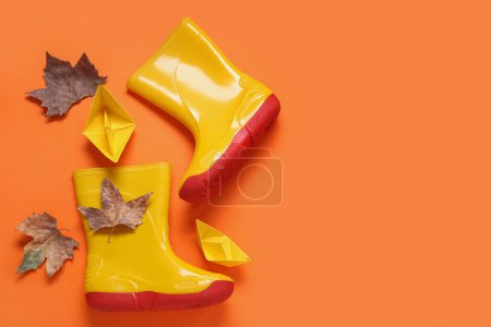 Foto de Botas de goma amarillas con hojas de otoño y barcos de papel sobre fondo naranja - Imagen libre de derechos