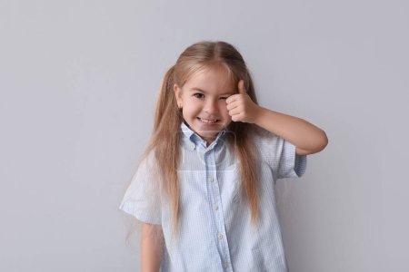 Photo for Happy little girl showing thumb-up on grey background - Royalty Free Image