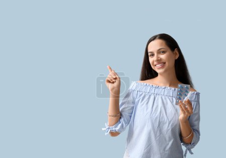 Téléchargez les photos : Jeune femme avec des gouttes nasales et des pilules pointant quelque chose sur fond bleu - en image libre de droit