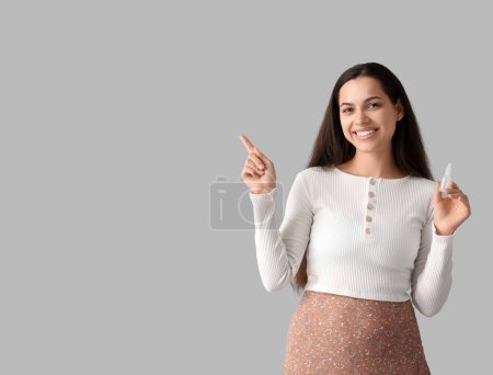 Téléchargez les photos : Jeune femme avec des gouttes nasales pointant quelque chose sur fond gris - en image libre de droit