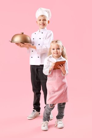 Téléchargez les photos : Mignon petit chef et serveuse sur fond rose. Célébration du Jour opposé - en image libre de droit