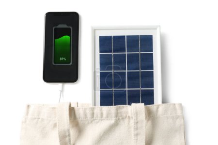 Foto de Bag with portable solar panel charging mobile phone on white background, closeup - Imagen libre de derechos