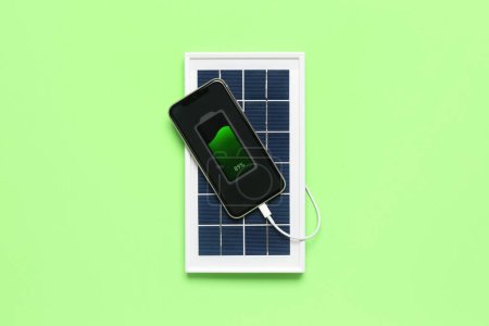 Foto de Portable solar panel charging mobile phone on green background - Imagen libre de derechos