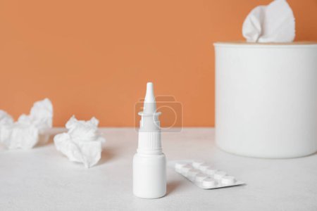Foto de Gotas nasales con pastillas y caja de tejido en la mesa cerca de la pared naranja, primer plano. Concepto de alergia - Imagen libre de derechos