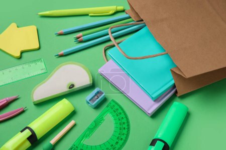 Foto de Composición con bolsa de papel y diferentes artículos de papelería sobre fondo verde, primer plano - Imagen libre de derechos