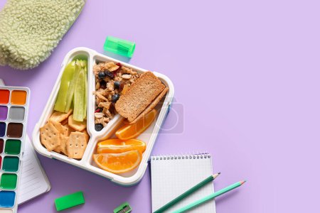 Foto de Almuerzo con deliciosa comida y diferentes artículos de papelería sobre fondo lila - Imagen libre de derechos