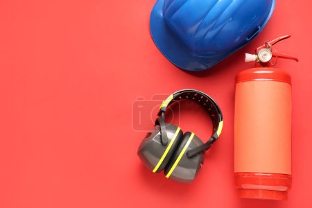 Foto de Extintor de incendios, protectores auditivos y casco sobre fondo rojo - Imagen libre de derechos