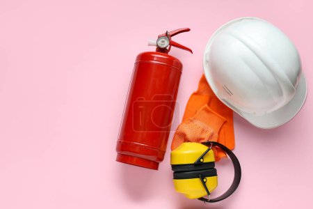Foto de Extintor de incendios, protectores auditivos, casco y guantes sobre fondo rosa - Imagen libre de derechos