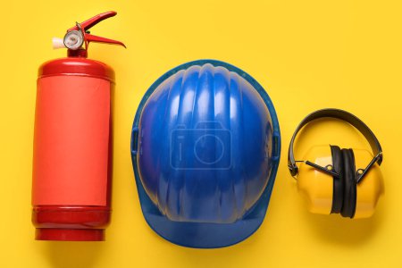 Foto de Extintor de incendios, protectores auditivos y casco sobre fondo amarillo - Imagen libre de derechos