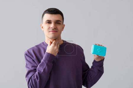 Photo for Young man with thyroid gland problem and pill box on light background - Royalty Free Image