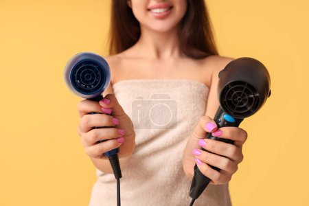 Photo for Beautiful young happy woman with towel and hair dryers on yellow background, closeup - Royalty Free Image