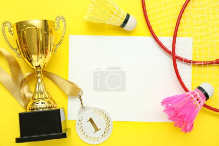 Photo for Blank card with gold cup, first place medal and badminton equipment on yellow background - Royalty Free Image