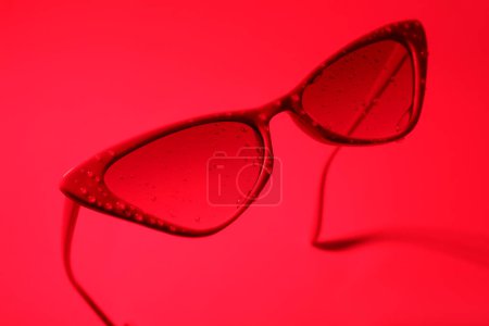 Téléchargez les photos : Lunettes de soleil élégantes avec gouttes d'eau sur fond rouge - en image libre de droit