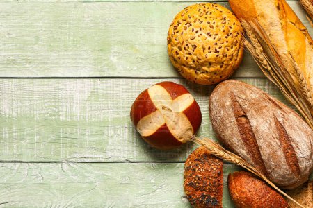 Photo for Different types of bread and wheat ears on green wooden table - Royalty Free Image