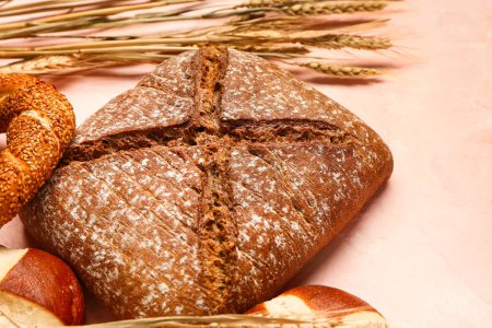 Photo for Fresh loaf of rye bread and wheat ears on pink table - Royalty Free Image