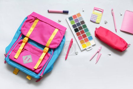 Foto de Mochila escolar colorida con acuarelas, calculadora y estuche de lápiz sobre fondo blanco - Imagen libre de derechos