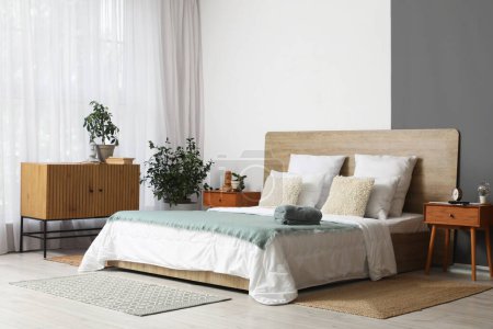 Interior of modern bedroom with wooden bed, houseplants and alarm clock on bedside table