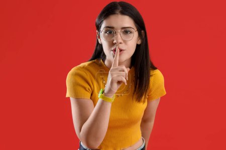 Téléchargez les photos : Jeune femme commérage montrant un geste de silence sur fond rouge - en image libre de droit