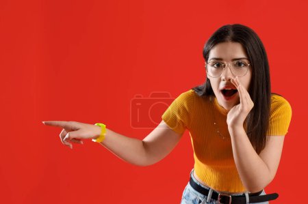 Photo for Young gossip woman pointing at something on red background - Royalty Free Image