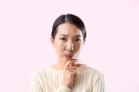 Photo for Portrait of thoughtful young Asian woman on pink background - Royalty Free Image