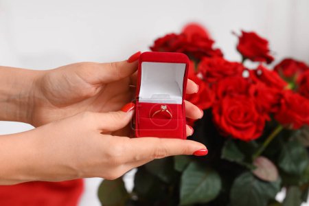 Foto de Manos femeninas sosteniendo caja con anillo de compromiso cerca de ramo de rosas, primer plano. Celebraciones del Día de San Valentín - Imagen libre de derechos