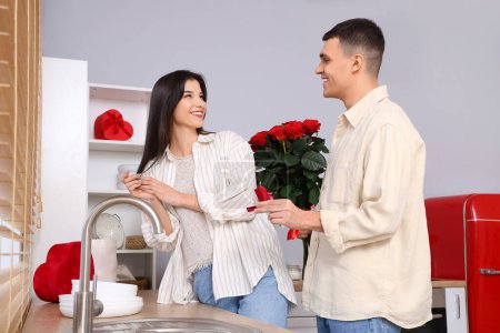 Foto de Joven con ramo de rosas proponiéndole matrimonio a su novia en la cocina. Celebración de San Valentín - Imagen libre de derechos