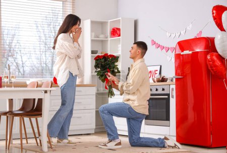 Foto de Joven proponiéndole matrimonio a su novia en la cocina. Celebración de San Valentín - Imagen libre de derechos