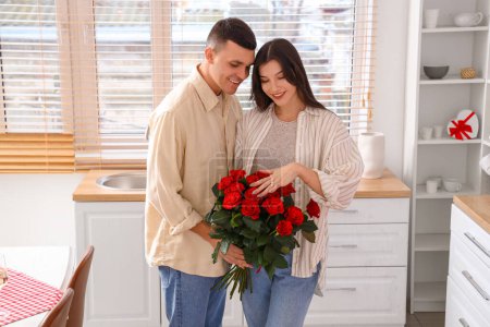Foto de Joven pareja comprometida con ramo de rosas en la cocina. Celebración de San Valentín - Imagen libre de derechos