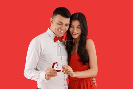 Foto de Pareja joven comprometida con anillo de boda sobre fondo rojo. Celebración de San Valentín - Imagen libre de derechos