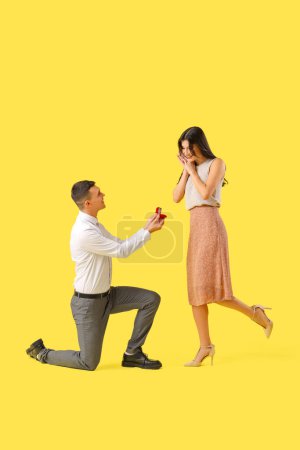 Foto de Joven proponiéndole matrimonio a su novia sobre fondo amarillo. Celebración de San Valentín - Imagen libre de derechos