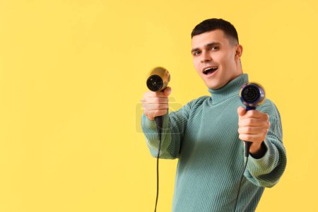Photo for Handsome young man with hair dryers on yellow background - Royalty Free Image