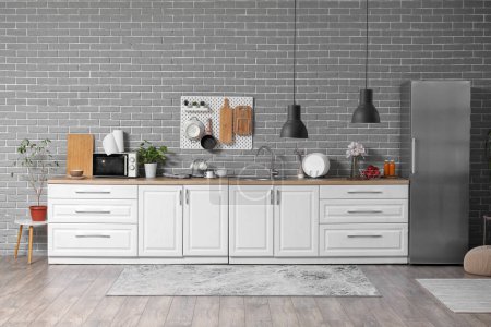 Foto de Interior de la cocina moderna con mostradores blancos y pegatina colgando en la pared de ladrillo gris - Imagen libre de derechos