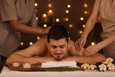 Photo for Young man getting massage from therapists in dark spa salon - Royalty Free Image