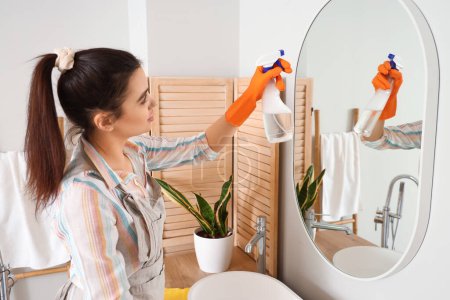Photo for Young woman cleaning mirror in her bathroom - Royalty Free Image