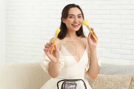 Téléchargez les photos : Belle jeune femme avec sac cosmétique plein de produits de maquillage et de brosses dans la chambre - en image libre de droit