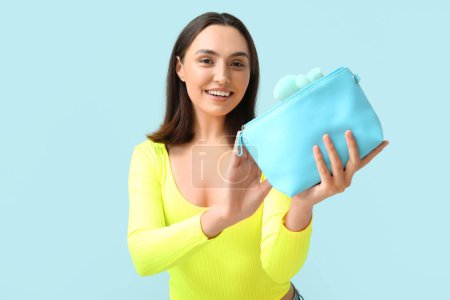 Téléchargez les photos : Belle jeune femme avec sac cosmétique plein de produits de maquillage sur fond bleu - en image libre de droit