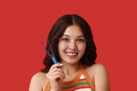 Téléchargez les photos : Heureuse jeune femme asiatique avec grattoir de langue sur fond rouge - en image libre de droit