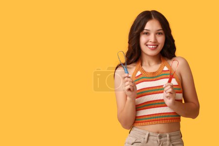Téléchargez les photos : Heureuse jeune femme asiatique avec grattoirs de langue sur fond jaune - en image libre de droit