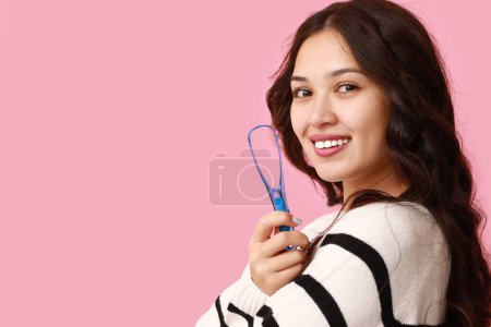 Téléchargez les photos : Heureuse jeune femme asiatique avec grattoir de langue sur fond rose - en image libre de droit