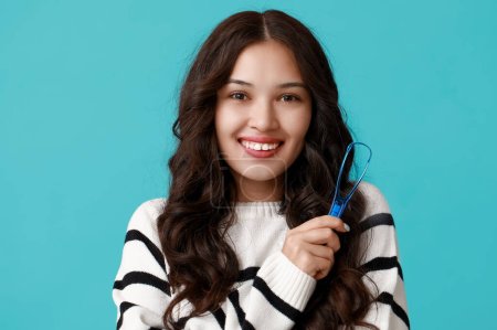 Téléchargez les photos : Heureuse jeune femme asiatique avec grattoir de langue sur fond bleu - en image libre de droit