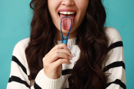 Téléchargez les photos : Belle jeune femme asiatique avec grattoir de langue sur fond bleu - en image libre de droit