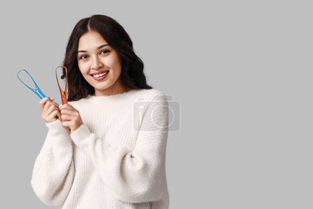 Photo for Happy young Asian woman with tongue scrapers on grey background - Royalty Free Image