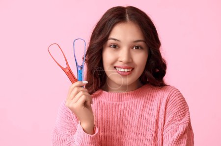 Téléchargez les photos : Heureuse jeune femme asiatique avec grattoirs de langue sur fond rose - en image libre de droit
